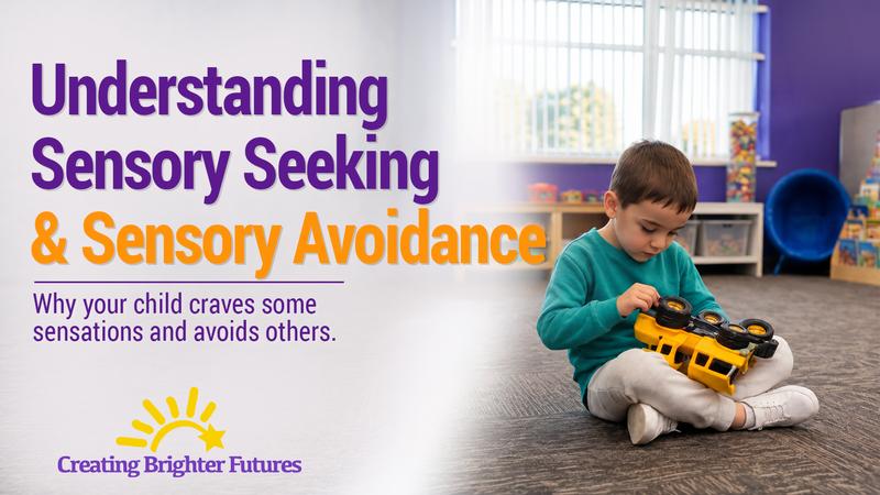 A young boy sits cross-legged on a classroom carpet, holding a yellow toy truck upside down and spinning its wheels, a common form of sensory-seeking play.